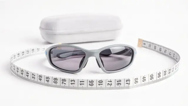 Sportliche Kindersonnenbrille neben Maßband und Etui als Thema Passform und Sitz für Eltern
