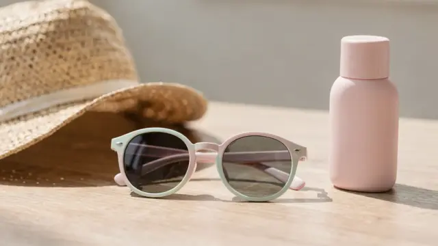 Polarisierte Kindersonnenbrille für Kinder auf einem Tisch mit Hut und Sonnencreme