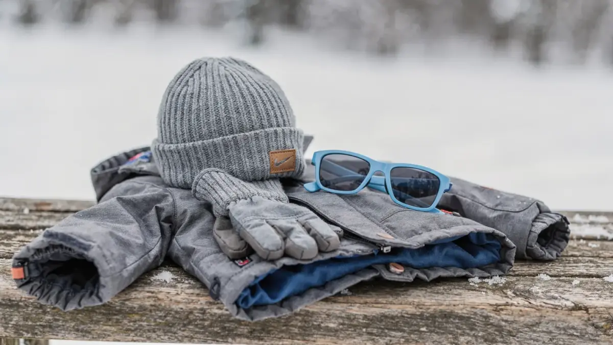Kindersonnenbrille im Winter neben Mütze und Handschuhen als Schutz für Kinderaugen