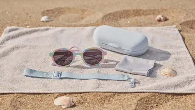 Sonnenbrillen-Zubehör am Strand für Kindersonnenbrillen: Etui, Putztuch und Band neben Kindersonnenbrillen.
