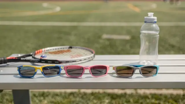 Kindersonnenbrille für Sport auf einer Sportbank mit Tennisracket und Wasserflasche